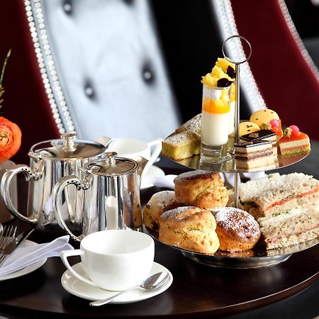 Macdonald Bath Spa Hotel Buitenkant foto The photo depicts an elegantly arranged afternoon tea setting. There is a tiered stand filled with a variety of treats, including scones, sandwiches, and small desserts like cakes and pastries. Accompanying this is a teapot and a cup on the table, su