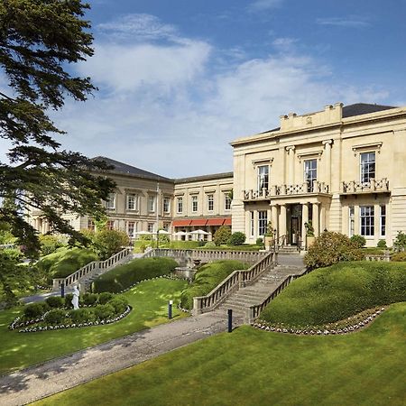 Macdonald Bath Spa Hotel Buitenkant foto The photo shows a grand building, likely a hotel or estate, surrounded by well-manicured gardens and lawns. The architecture appears elegant, with multiple stories and large windows. There are steps leading up to the entrance, and the setting include