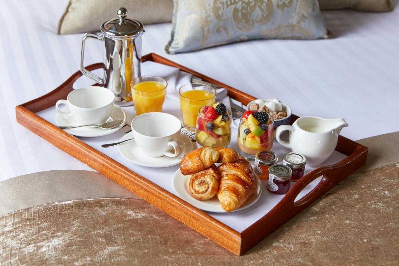 Macdonald Bath Spa Hotel Buitenkant foto The photo shows a wooden tray arranged with a delightful breakfast spread. On the tray, there are two cups, a coffee pot, and several glasses of orange juice. There's also a small bowl of mixed fruit, featuring various colorful pieces. Additionally, 