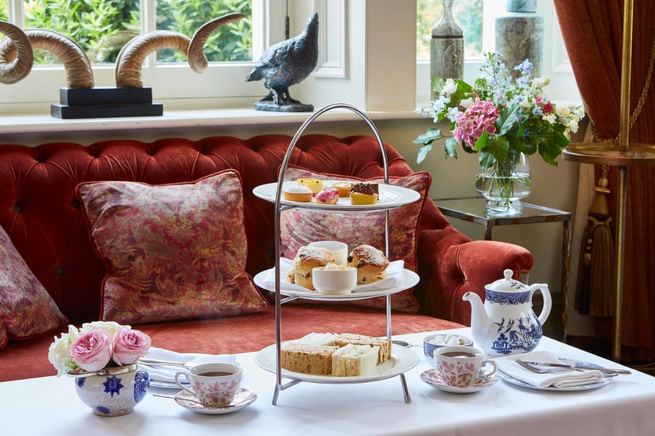 Macdonald Bath Spa Hotel Buitenkant foto The photo showcases an elegant afternoon tea setting. In the foreground, there is a three-tiered serving stand filled with various pastries and scones, including some topped with cream and fruit. Surrounding the stand is a beautifully arranged table 