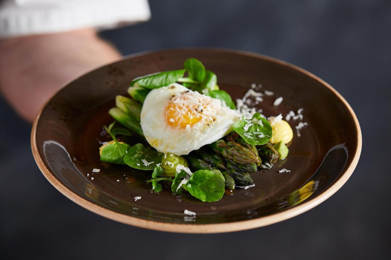 Macdonald Bath Spa Hotel Buitenkant foto The photo shows a plate of beautifully arranged food, featuring a poached egg on top of a mix of fresh greens. The greens include asparagus, lettuce, and possibly some herbs, garnished with a sprinkle of grated cheese or a similar topping. The dish i
