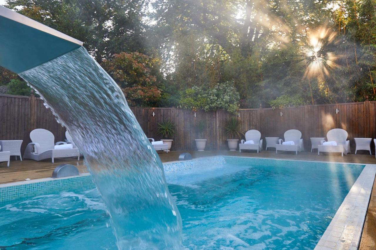 Macdonald Bath Spa Hotel Buitenkant foto The photo shows a tranquil swimming pool surrounded by greenery. Water is cascading from a feature into the pool, creating a refreshing effect. In the background, there are white lounge chairs positioned neatly along the poolside, inviting relaxation