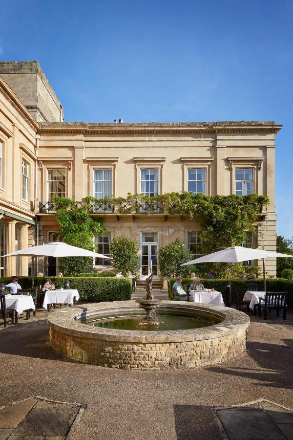 Macdonald Bath Spa Hotel Buitenkant foto The photo depicts a charming outdoor dining area of a classic-looking building with elegant architecture. The structure features large windows and is adorned with greenery, including climbing plants. In the foreground, there is a circular fountain, a