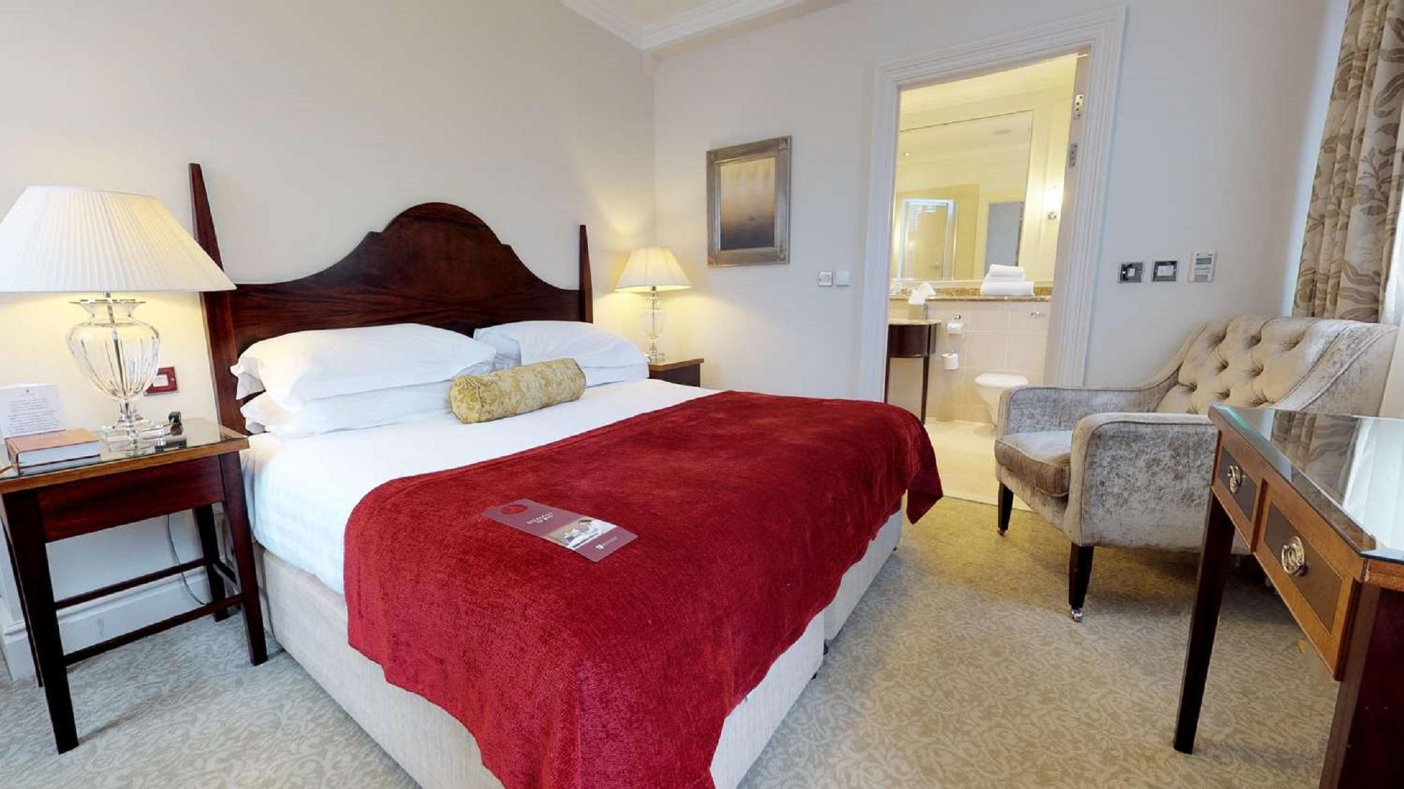 Macdonald Bath Spa Hotel Buitenkant foto The photo shows a well-furnished hotel room. In the center, there is a large bed with white linens and a red throw blanket. A decorative pillow is placed on the bed. On either side of the bed, there are bedside tables with lamps. To the right, there 