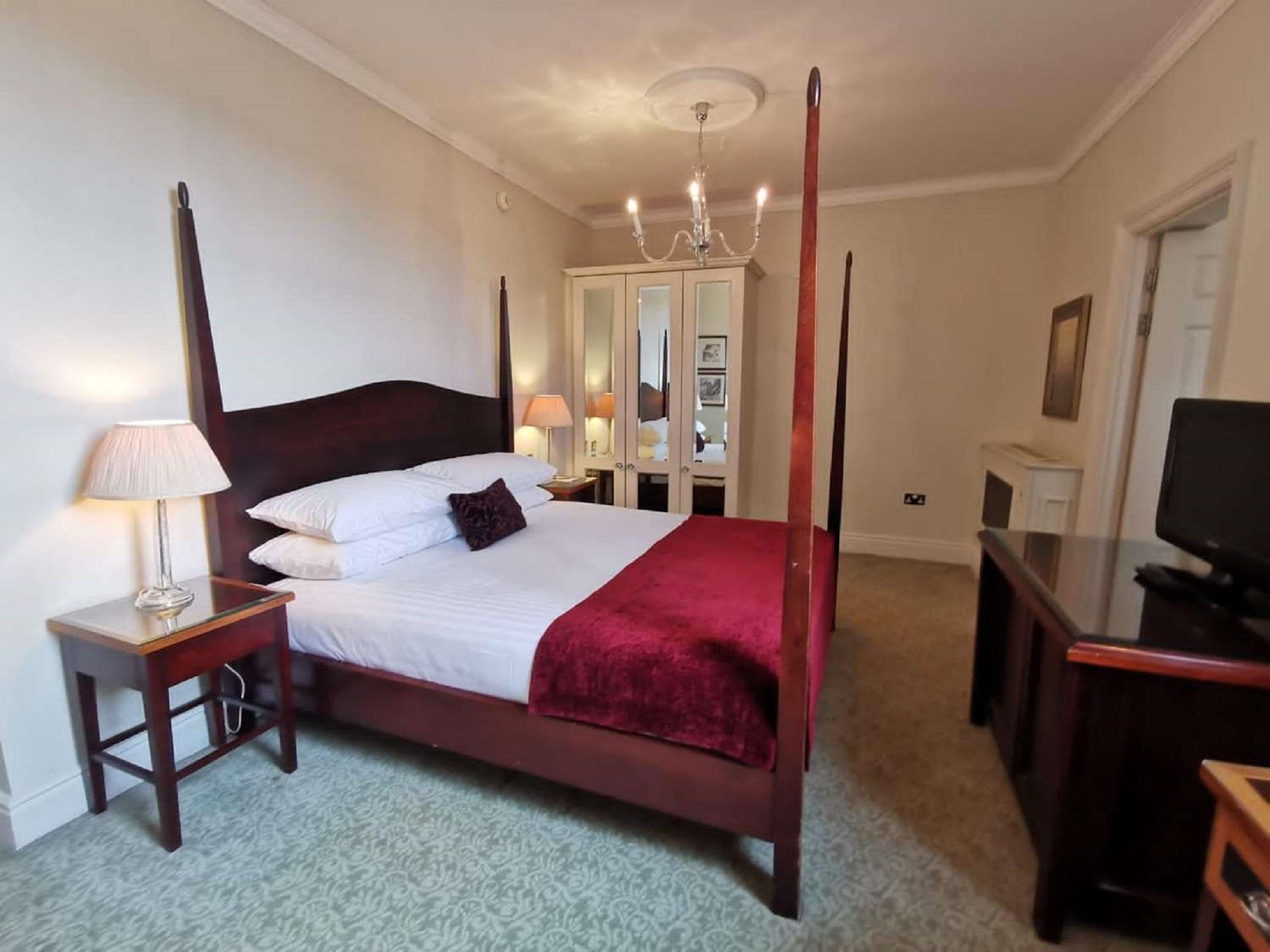 Macdonald Bath Spa Hotel Buitenkant foto The photo shows a well-decorated bedroom featuring a four-poster bed with white pillows and a burgundy throw. There are two bedside lamps on wooden nightstands on either side of the bed. A large wardrobe or mirror cabinet is visible in the background