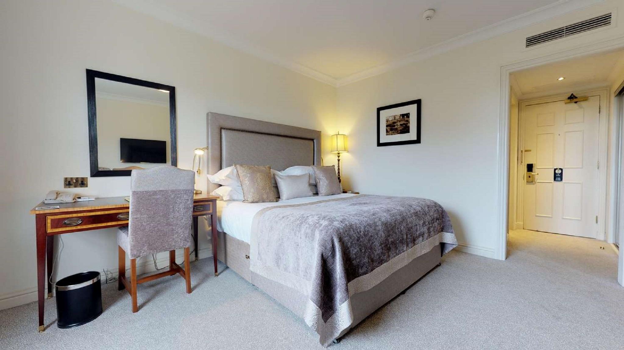 Macdonald Bath Spa Hotel Buitenkant foto The photo shows a well-decorated hotel room. In the center, there's a comfortable bed with plush bedding and decorative pillows. A bedside table with a lamp is positioned next to the bed. To the left, there's a small desk with a chair, accompanied by