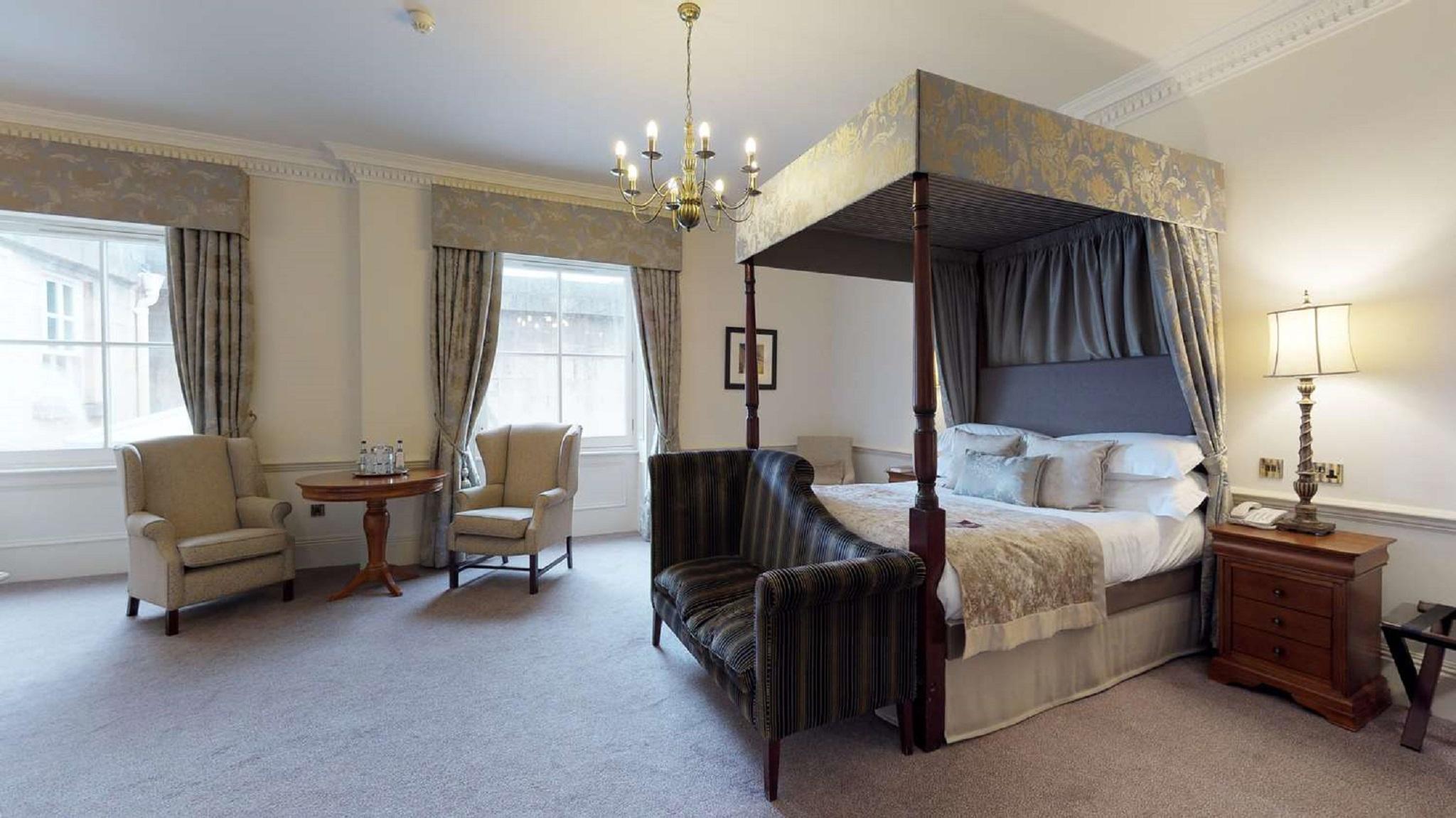 Macdonald Bath Spa Hotel Buitenkant foto The photo shows a stylish hotel room featuring a four-poster bed with a decorative canopy. The bed is positioned prominently in the center, surrounded by plush bedding. To the side, there are two armchairs with a small round table between them, creat