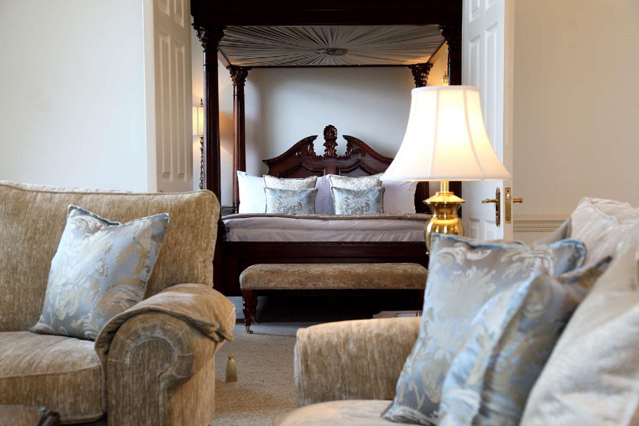 Macdonald Bath Spa Hotel Buitenkant foto The photo shows a beautifully decorated room featuring a four-poster bed in the background. The bed has a wooden frame with a rich design, and it is adorned with plush bedding and pillows. In the foreground, there are comfortable sofas with decorativ