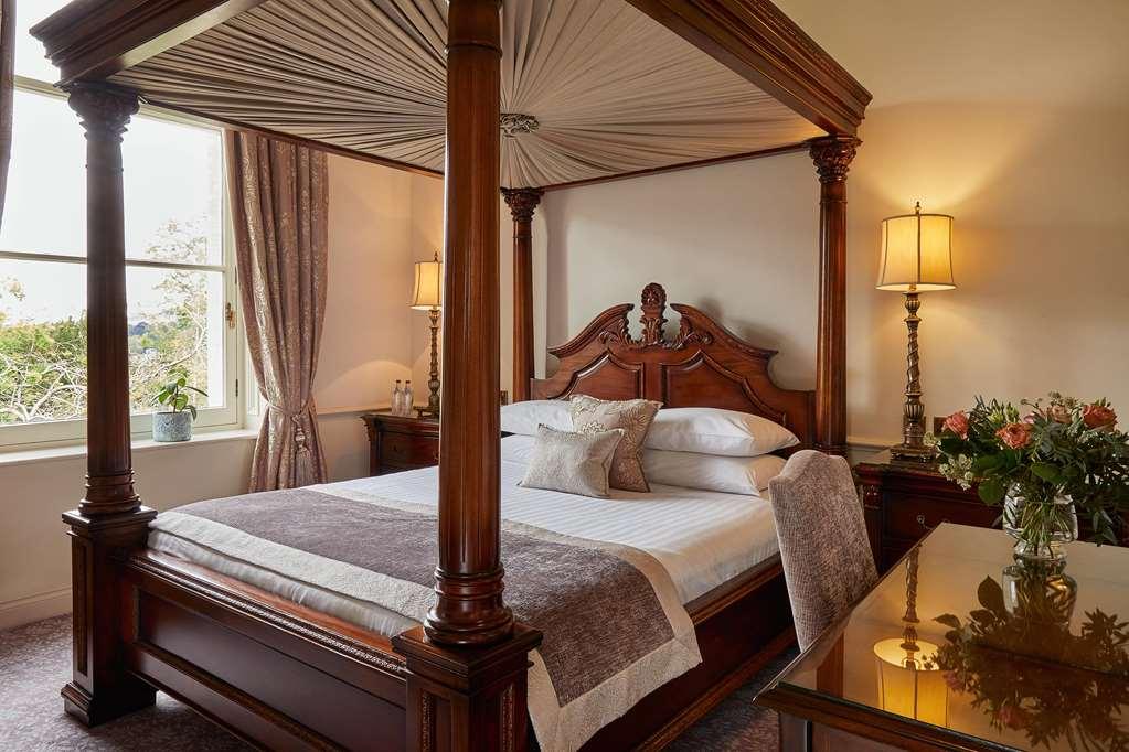 Macdonald Bath Spa Hotel Kamer foto The photo shows a beautifully designed bedroom featuring a four-poster bed made of dark wood. The bed has an elaborately carved headboard and is adorned with a light-colored bedding set. Above the bed, there is a canopy that adds an elegant touch. On