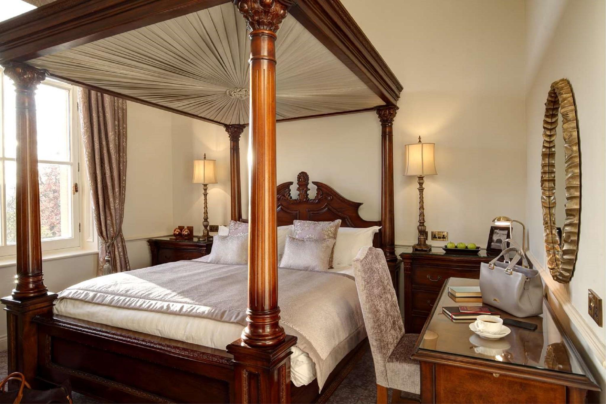 Macdonald Bath Spa Hotel Buitenkant foto The photo shows a beautifully designed bedroom featuring a four-poster bed with a canopy. The bed is adorned with white linens and decorative pillows. On either side of the bed, there are bedside tables with lamps providing warm lighting. Large windo