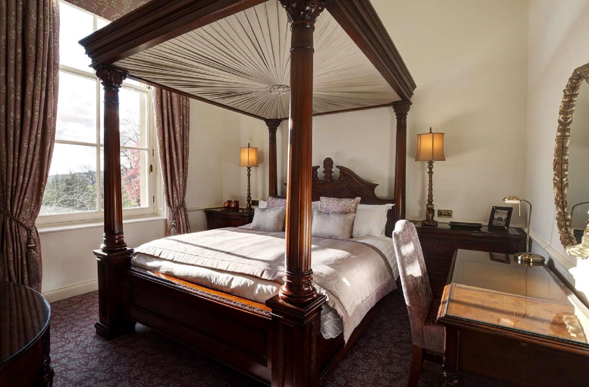 Macdonald Bath Spa Hotel Buitenkant foto The photo shows a well-decorated bedroom featuring a four-poster bed with an elegant wooden frame. The bed is dressed with light-colored linens and several decorative pillows. On either side of the bed, there are matching bedside lamps that provide s