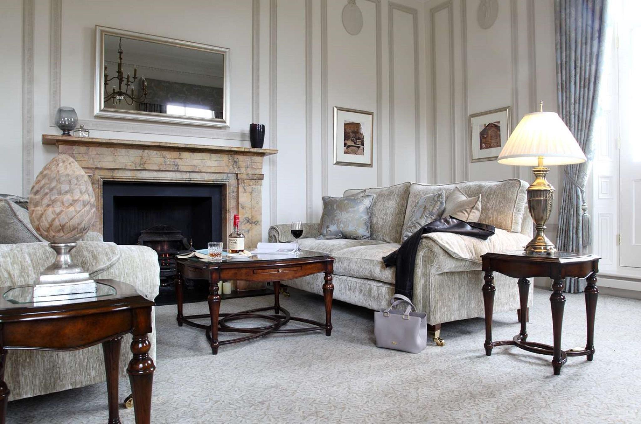 Macdonald Bath Spa Hotel Buitenkant foto The photo shows a stylish living room. It features a plush light-colored sofa adorned with decorative pillows. Next to the sofa, there is a small wooden coffee table with a decorative item and a bottle of wine, along with a glass. A larger wooden tab