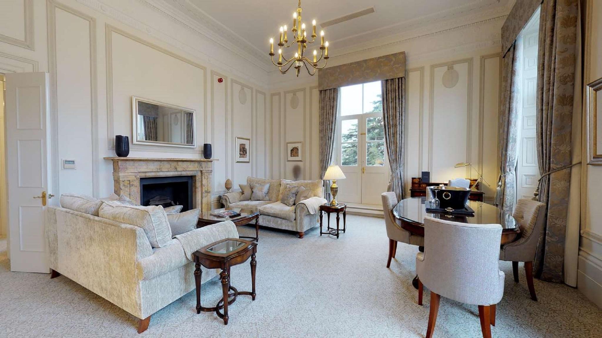 Macdonald Bath Spa Hotel Buitenkant foto The photo shows an elegant living room with a classic design. It features a large chandelier hanging from the ceiling, providing soft lighting. The walls are adorned with decorative moldings and have a light color. 

In the center, there are two plus