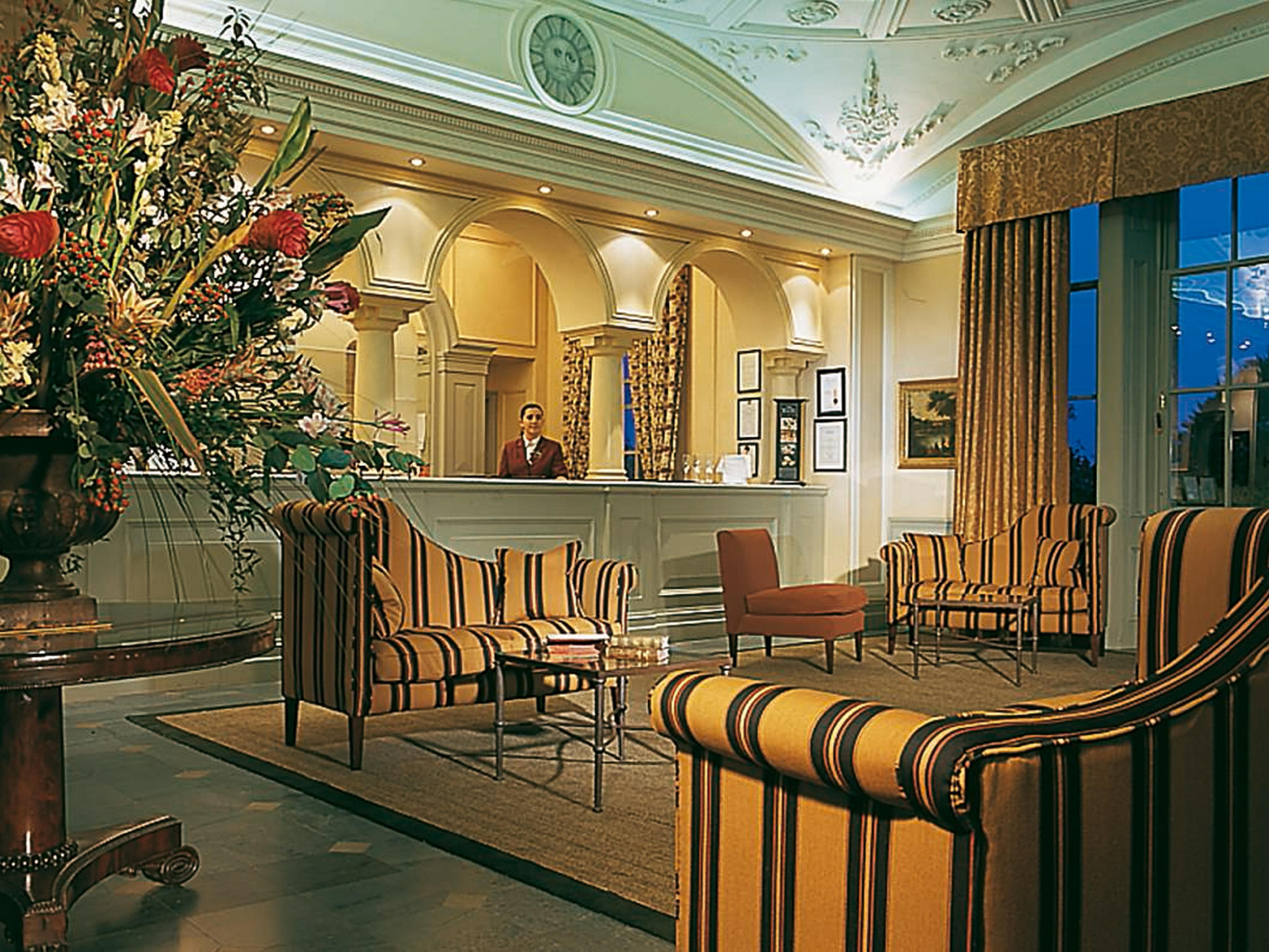 Macdonald Bath Spa Hotel Buitenkant foto The photo shows an elegant hotel lobby. The area features a reception desk with a staff member behind it. Surrounding the reception are comfortable seating arrangements, including striped armchairs and a brown chair. A large vase with an elaborate fl
