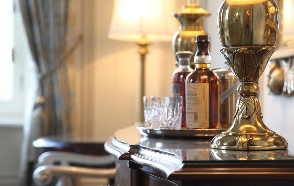 Macdonald Bath Spa Hotel Buitenkant foto The photo features an elegant interior scene that includes a polished wooden bar or table. On the surface, there are several bottles of liquor, likely whiskey, each with a distinctive label. A glass, possibly for drinking, is positioned near the bott