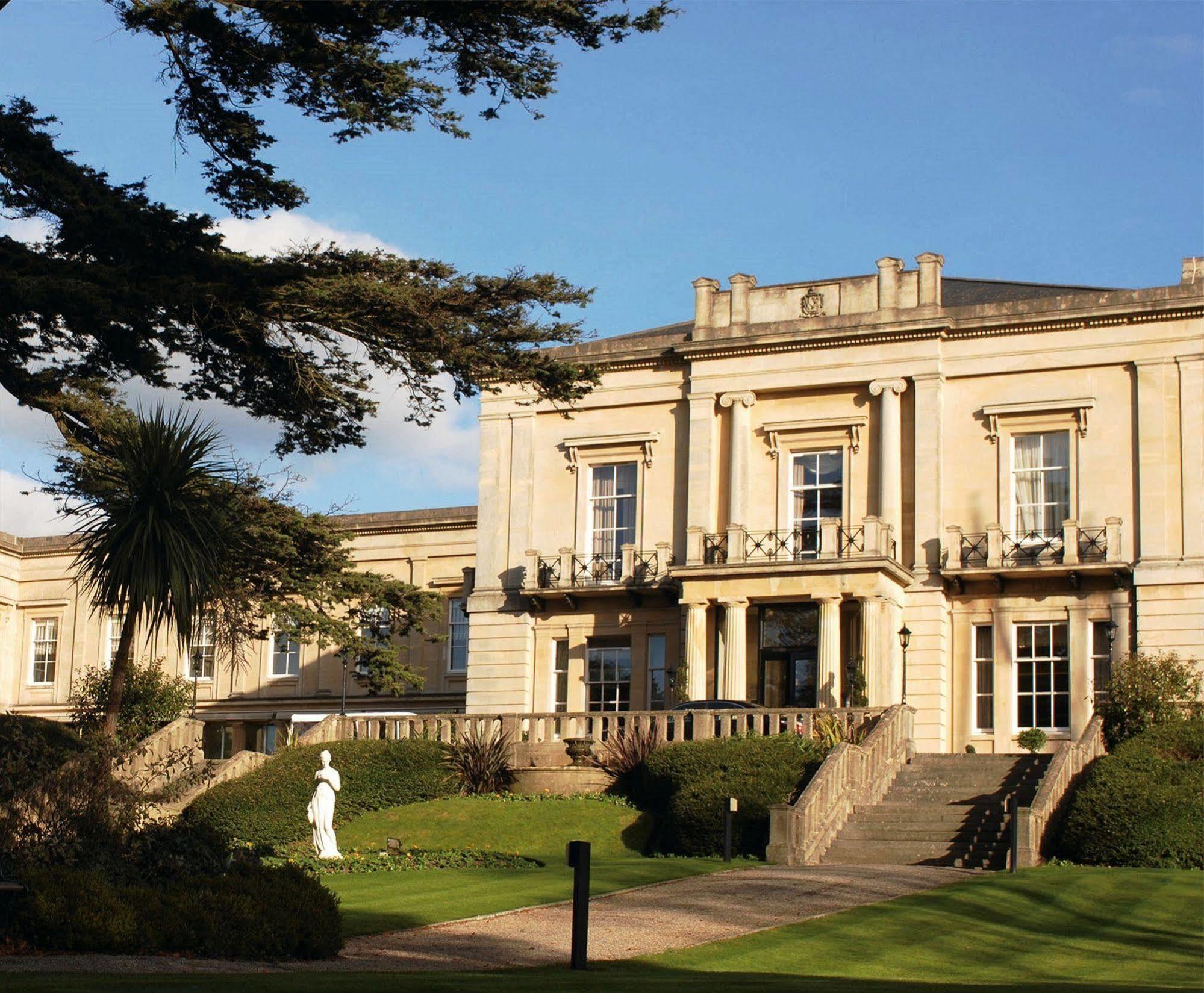 Macdonald Bath Spa Hotel Buitenkant foto The photo shows an elegant building with classical architecture, featuring large windows and decorative elements. The facade is light-colored, and there are several balconies. In front of the building, there is a landscaped area with greenery, includ